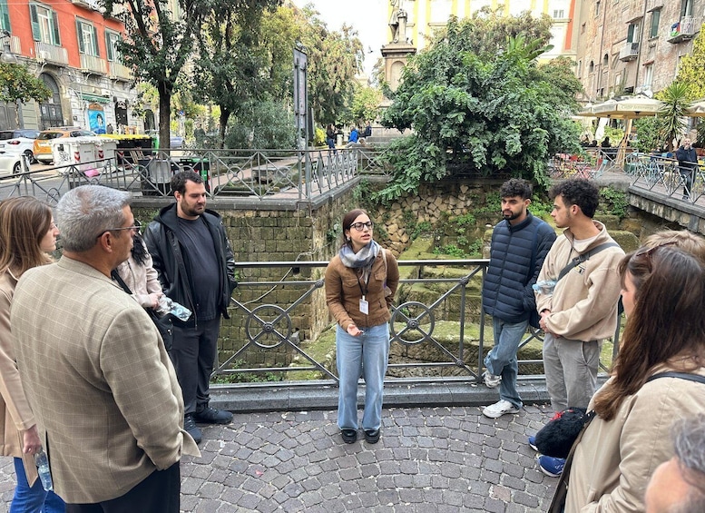 A group of people standing on a cobblestone path in an urban park with a canal and buildings in the background. 3