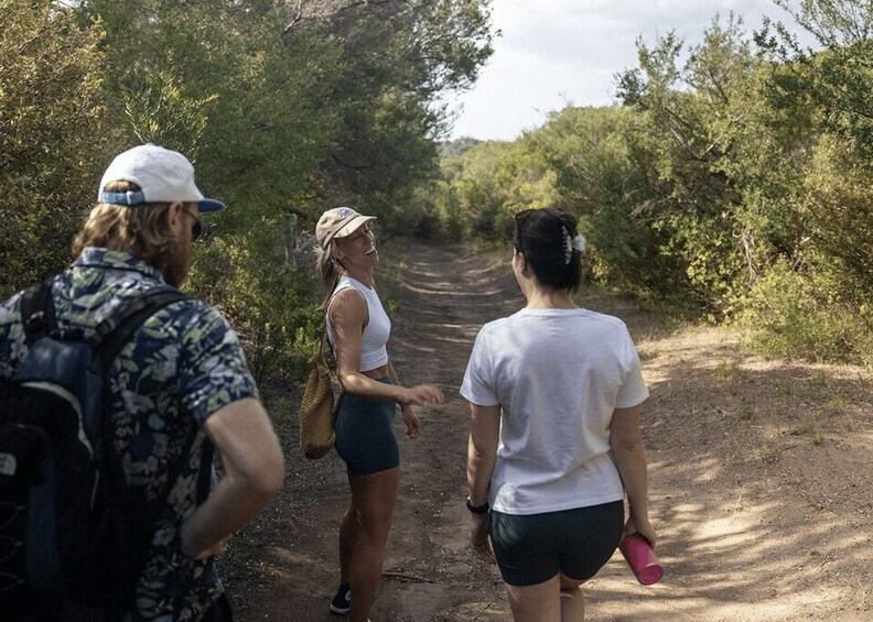 Three people walking on a dirt path surrounded by greenery. 2