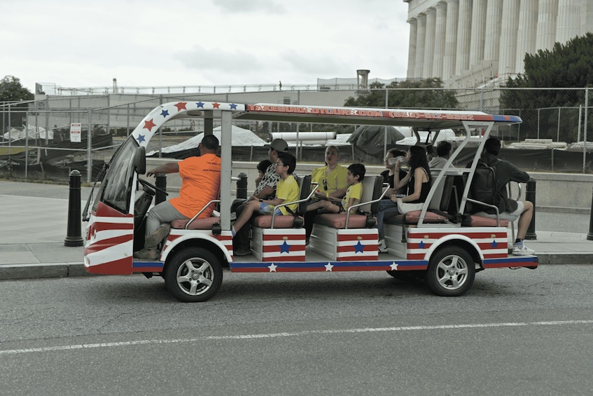 A tourist bus with a patriotic design, parked on a street with a large building in the background. 4