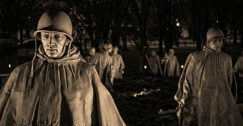 A nighttime scene with statues of soldiers in uniform, some with helmets and others with caps, standing in a park-like setting. 3