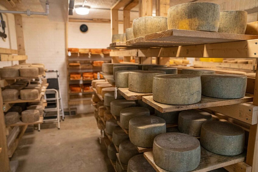 A cheese aging room with wooden shelves stacked with large wheels of cheese. 3
