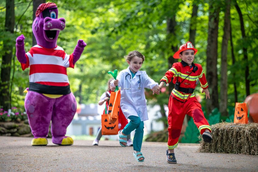 A person in a purple costume, a child in a white coat, and a child in a red and yellow costume running in a park. 2