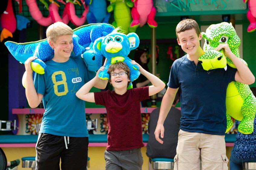 Three people holding plush toys, one blue monkey and one green dinosaur, in a colorful indoor setting. 3