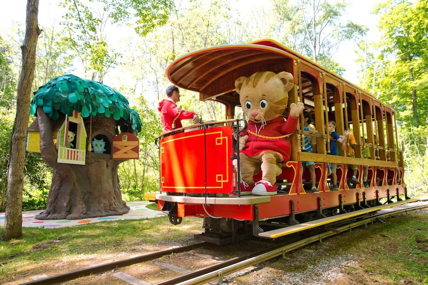A red train with a bear mascot, a treehouse, and a forested area. 2