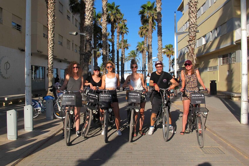 A group of people on bicycles with signs that read 'DODO' in a sunny urban setting with palm trees and buildings. 1