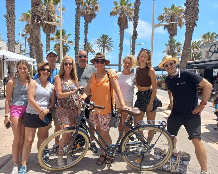 A group of people standing outdoors with bicycles, palm trees, and a clear sky. 5