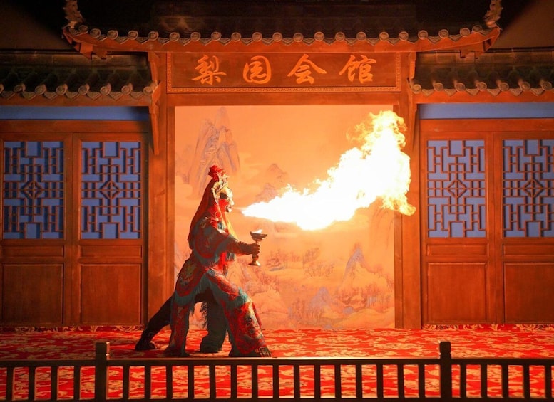 A person in traditional attire holding a flaming object in front of a wooden structure with Chinese characters. 1