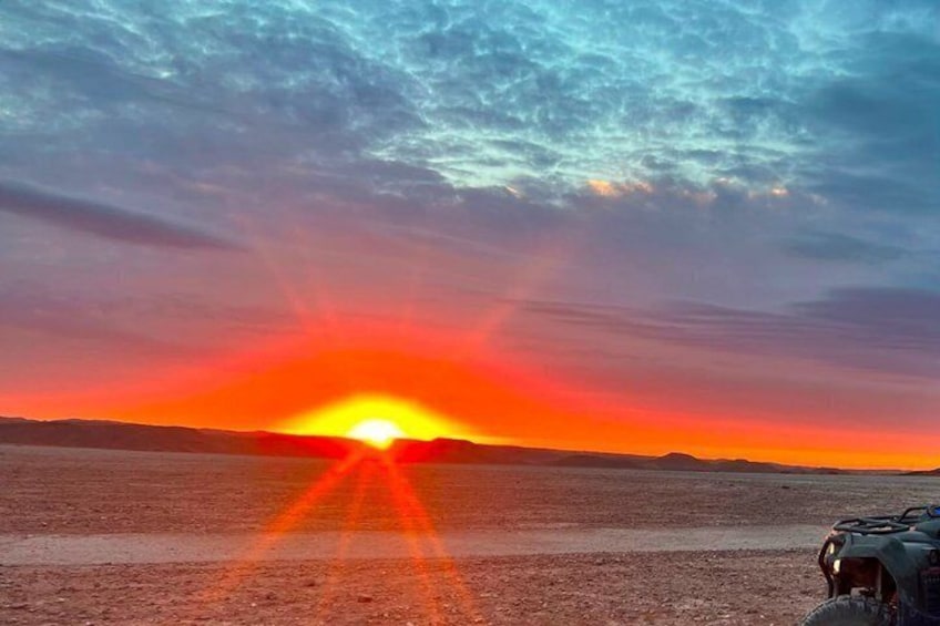 Een zonsondergang boven een vlak landschap, met een voertuig op de voorgrond. 2