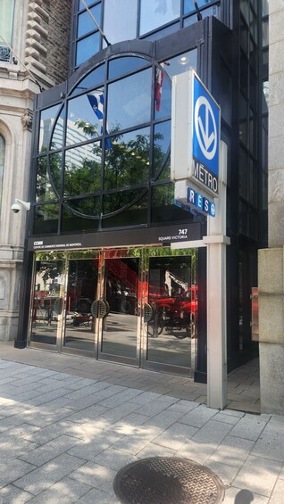 A modern building with a glass facade, a blue sign with 'METRO' and 'RES' on it, and the address '747 SQUARE-VICTORIA'. 1