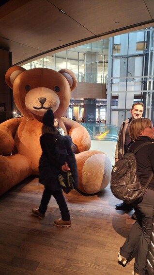 A large indoor sculpture of a bear, a glass building, and people walking. 3