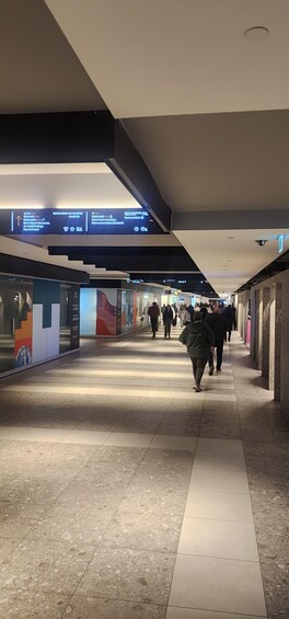 A corridor with overhead directional signs, tiled flooring, and people walking. 2