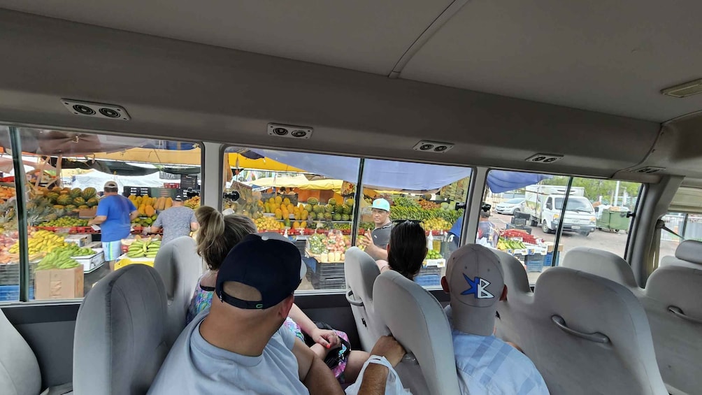 A vehicle interior with passengers looking out at a fruit market. 3