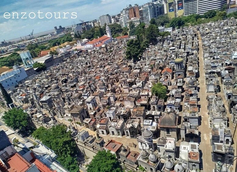 A densely packed cemetery with numerous tombs and mausoleums, surrounded by urban buildings and greenery. 1
