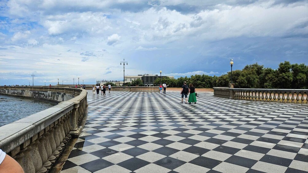 A checkered promenade with a water body on one side, a bridge, and a distant building. 5