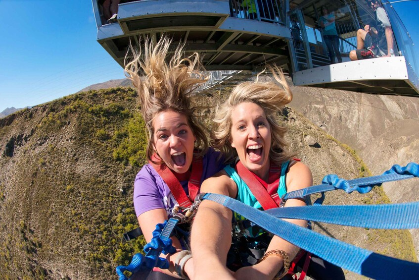Two people bungee jumping with harnesses and safety gear, overlooking a mountainous landscape. 3