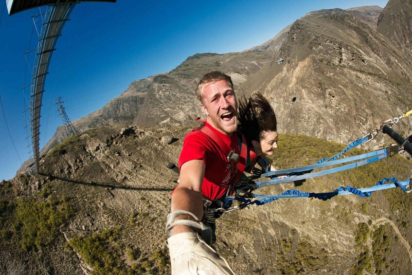 A person bungee jumping with safety harnesses, with a mountainous landscape in the background. 2