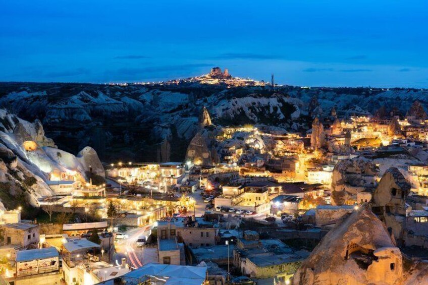 A town at dusk with illuminated buildings, snow-covered hills, and a prominent dome structure. 4