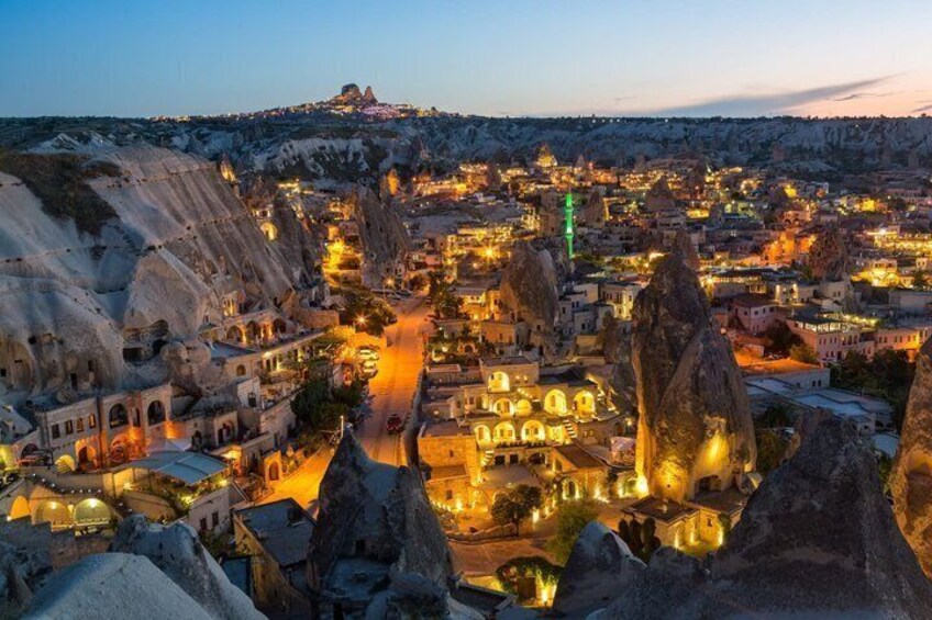 A town with unique rock formations and illuminated buildings at dusk. 1