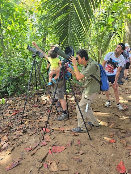 A group of people using telescopes in a forested area with fallen leaves on the ground. 2