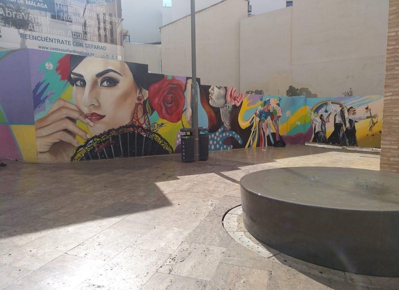 A mural with vibrant colors and abstract figures, a round concrete structure, and a tiled pavement. 4