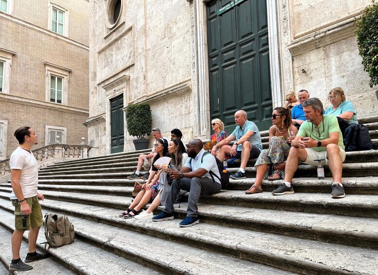 A group of people sitting on stone steps in front of a building with classical architecture. 3