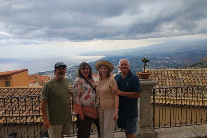 Four people standing on a balcony with a cityscape and cloudy sky in the background. 5