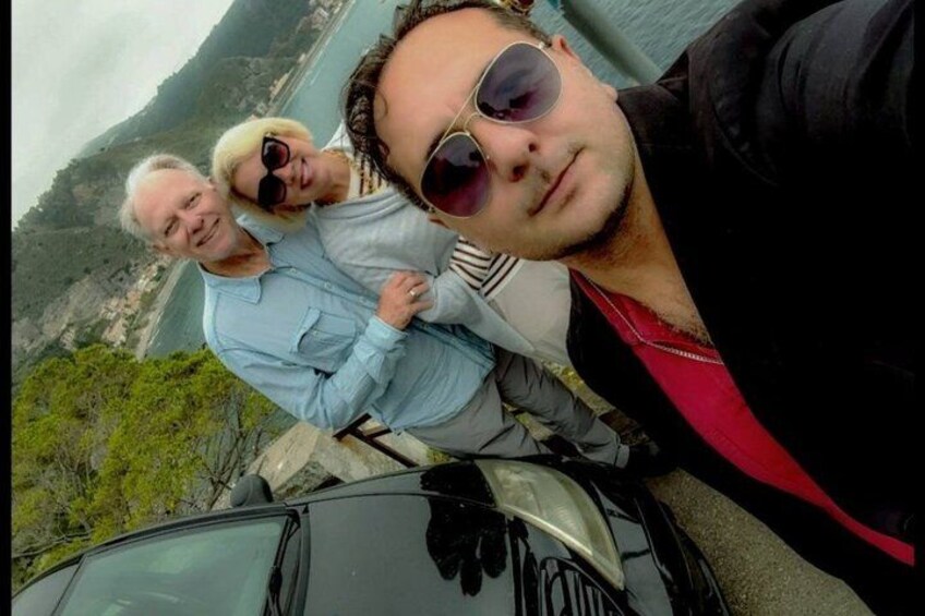Three people standing by a car with a mountainous landscape in the background. 2