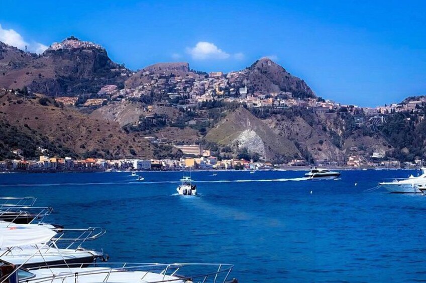 A coastal town with boats docked, a mountain in the background, and clear blue water. 5