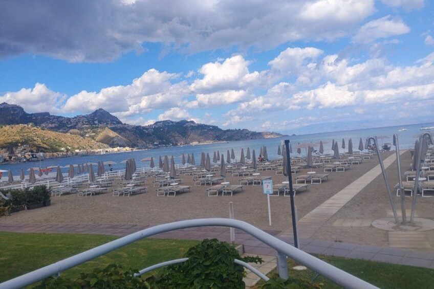 Een strand met rijen ligbedden en parasols, een heldere lucht en bergen op de achtergrond. 2