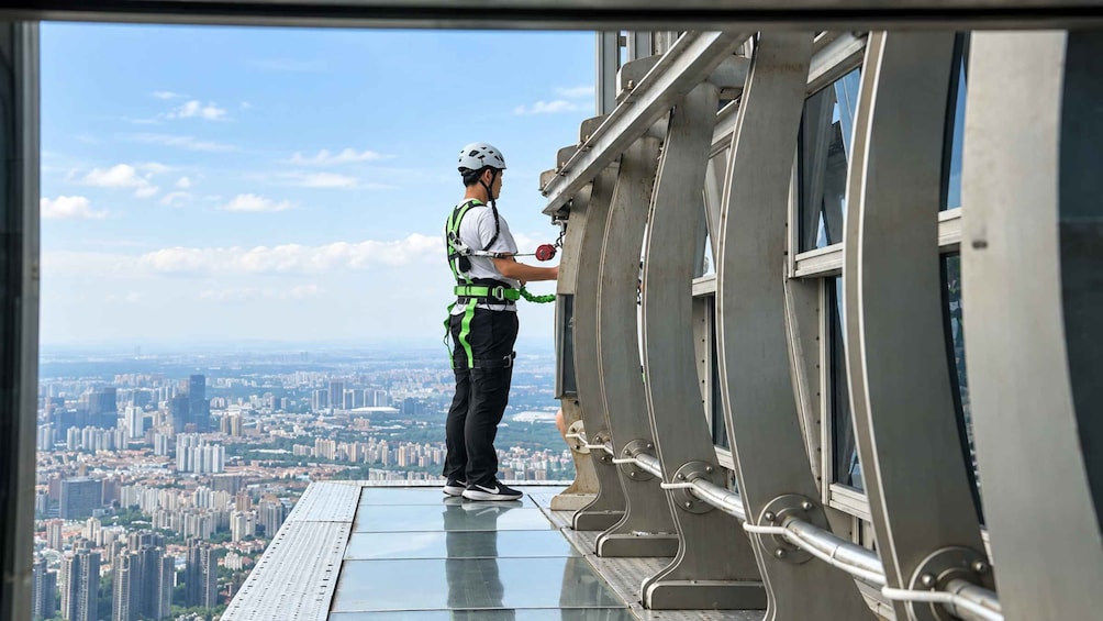 A person on a high-rise window ledge, wearing safety gear, overlooking a cityscape. 2