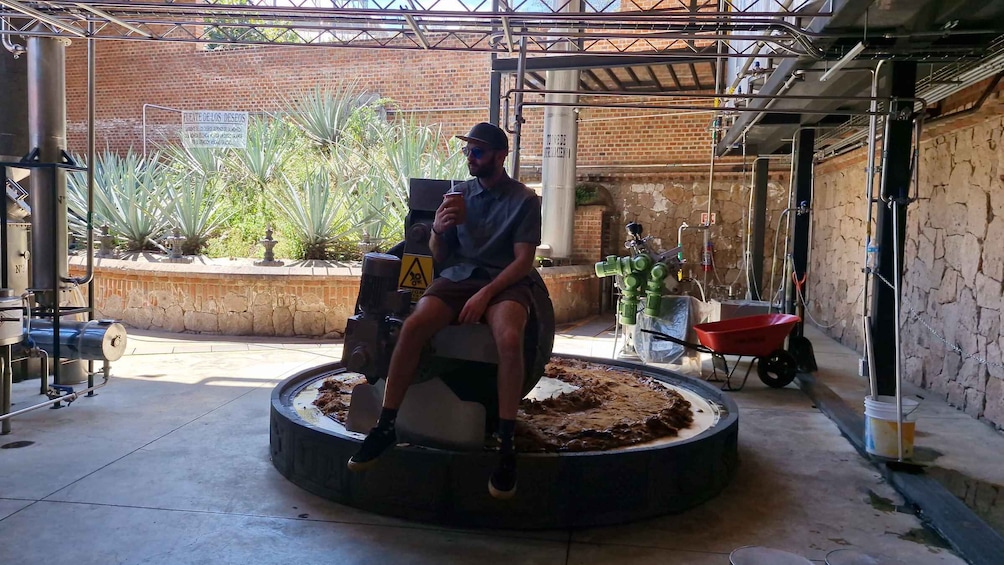 A person sitting on a circular platform in an industrial setting with brick walls, metal structures, and potted plants. 4