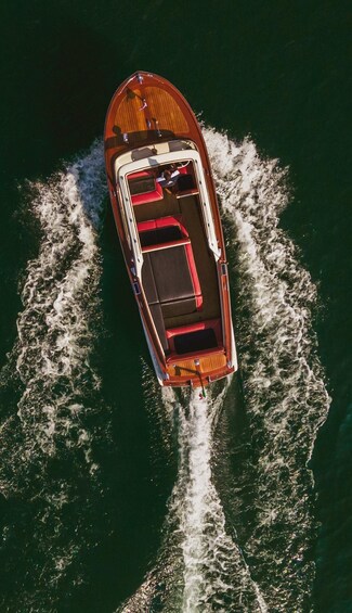 An aerial view of a wooden boat with a cabin and red seating, moving through water. 1