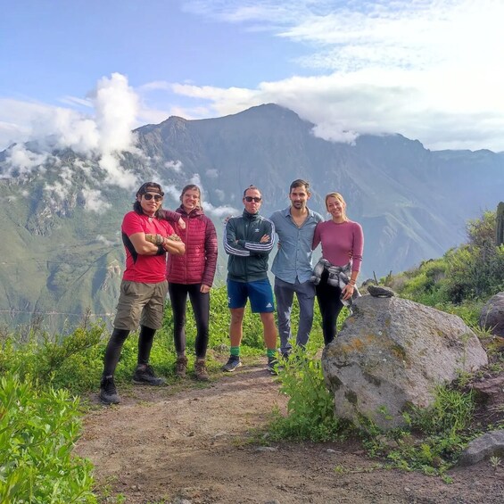 A group of hikers on a mountain trail with a view of a mountain range and clouds. 2