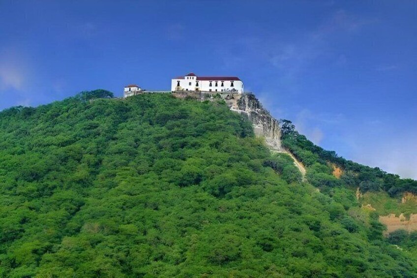 Un edificio bianco su una collina, con tetto rosso, circondato da un fitto bosco verde. 5