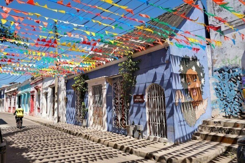 Una strada con bandiere colorate, un edificio blu con una maschera decorativa e un marciapiede a motivi. 4