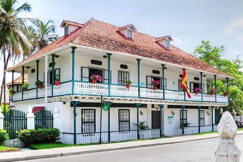 Un edificio in stile coloniale di due piani, con balconi, un tetto in tegole rosse e una bandiera. 3