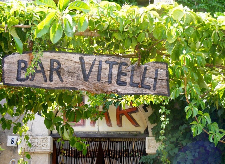 A rustic wooden sign with 'BAR VITELLI' written on it, hanging above a building entrance. 4