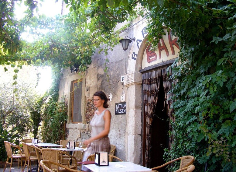 An outdoor café with wicker tables and chairs, a stone wall, and a sign reading 'BAK'. 2