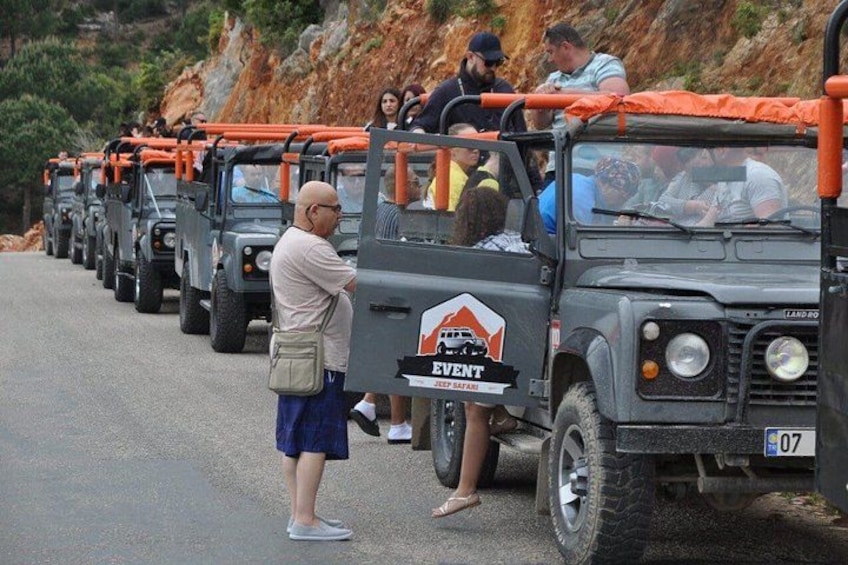 A line of off-road vehicles with orange tarps, parked on a road with people standing beside them. 5