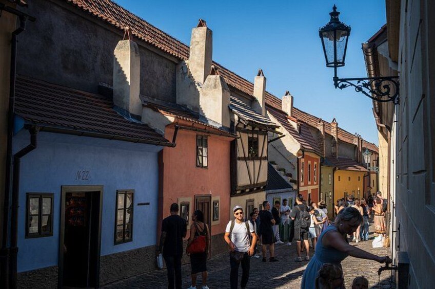 En kullerstensgata kantad av historiska byggnader, en folkmassa och en gatlykta. 2