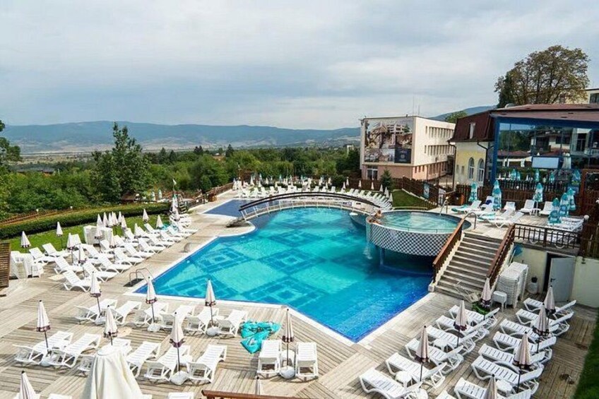 A swimming pool with lounge chairs and umbrellas, surrounded by buildings and greenery. 4