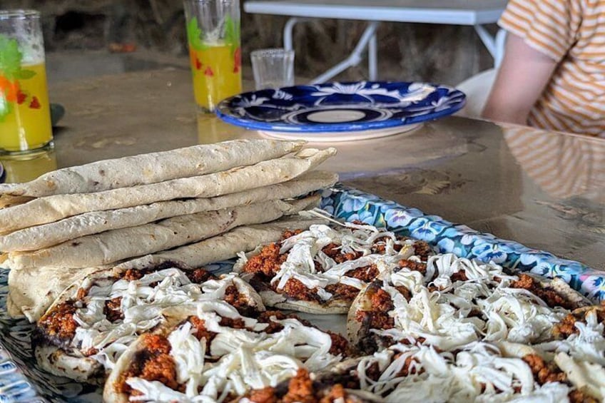 A tray of flatbreads and a dish of meat with shredded white topping, possibly cheese, on a table. 2