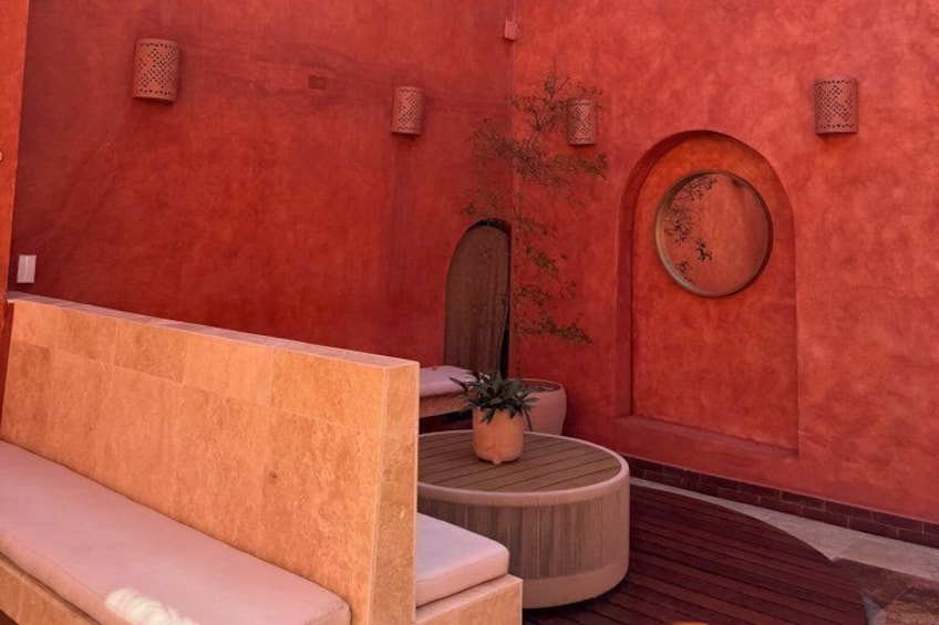 A red-walled room with a bench, a round table, and a potted plant. 2