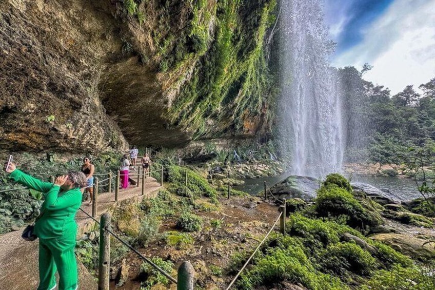 Ein Wasserfall stürzt eine Klippe hinab, umgeben von üppiger Vegetation und einer Aussichtsplattform mit Personen. 4