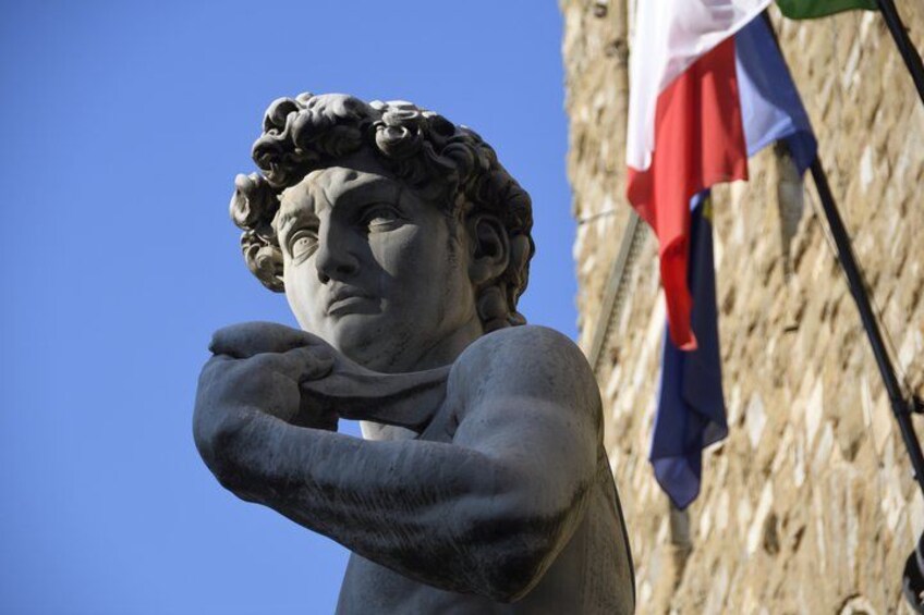 A statue with a draped cloth, set against a clear blue sky and a stone wall with a flag. 4