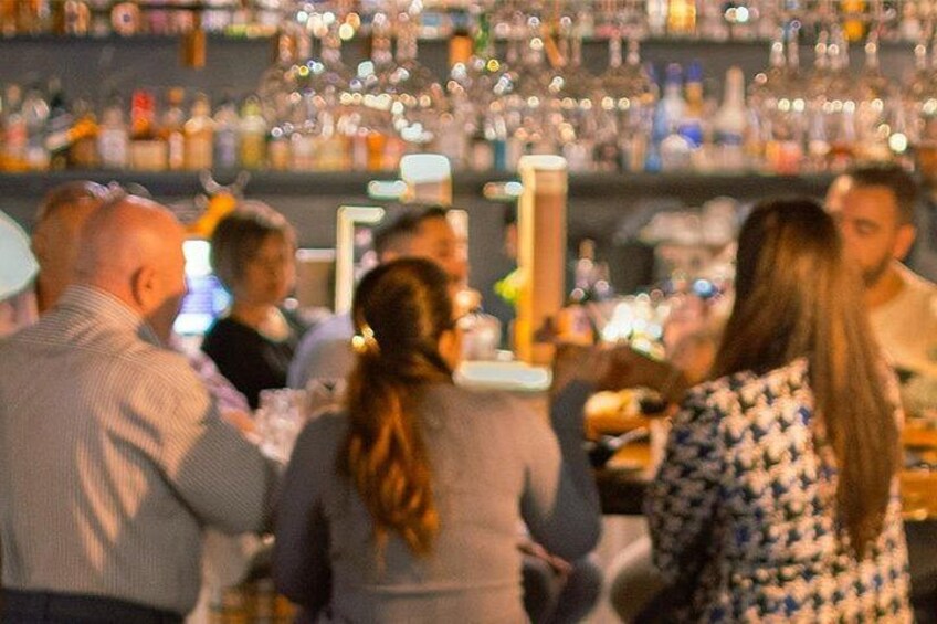A bar with people seated, bottles, and glasses on shelves. 1