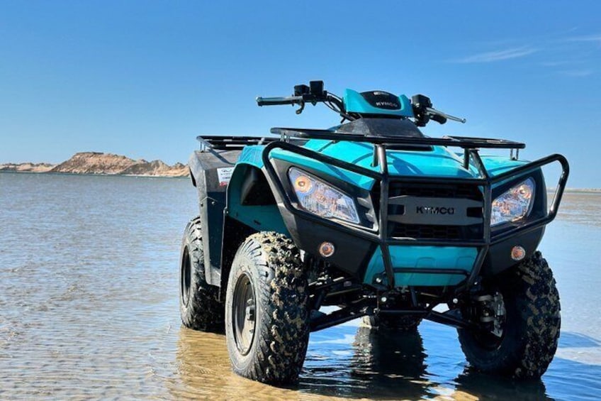 Un véhicule tout-terrain bleu sur une étendue d’eau, avec une côte rocheuse en arrière-plan. 3