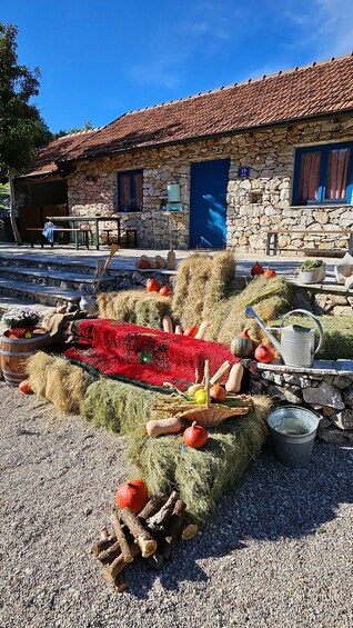 A rustic stone building with a tiled roof, hay bales, pumpkins, and a red blanket on the ground. 4