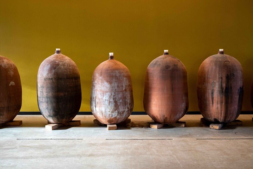 Five large, cylindrical ceramic pots with handles, standing on wooden blocks against a yellow wall. 4