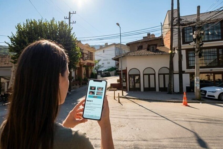A person holding a smartphone with a map application, standing on a street with buildings and a parked car. 5
